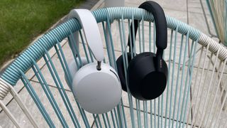 White Sonos Ace and black Sony WH-1000XM5 over-ear headphones hanging side-by-side on the back of a chair.