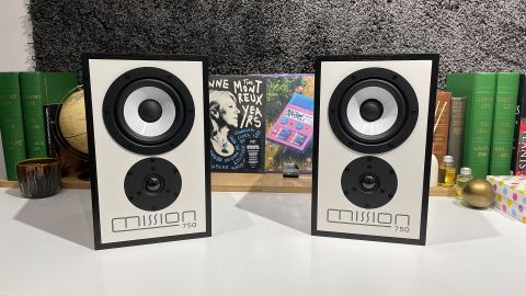 Mission 750 stereo speakers on white table in front of busy shelf